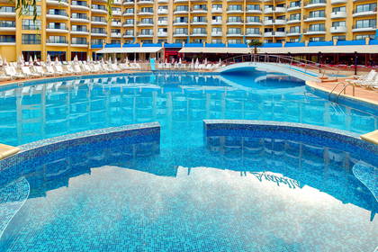 Basen hotelowy z leżakami i budynkiem w tle.