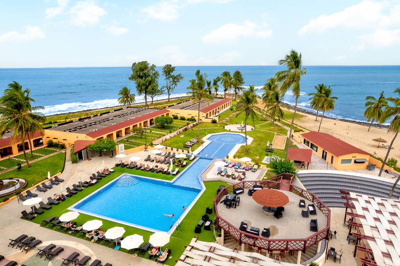 Kurort z basenami i palmami, widok z góry. W tle plaża i budynki.