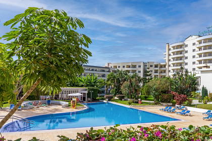 Hotelowy basen z leżakami i palmami. W tle budynek hotelu.