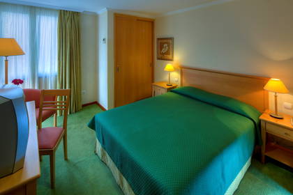 Pokój hotelowy z łóżkiem, szafkami nocnymi i telewizorem.