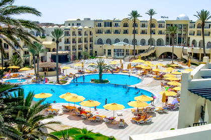 Kompleks hotelowy z basenem otoczonym palmami.