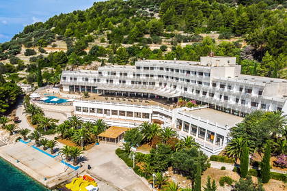 Biały hotel z basenem i palmami na wybrzeżu, widok z lotu ptaka.