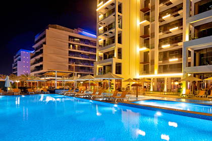Oświetlony basen hotelowy nocą z leżakami i parasolami.
