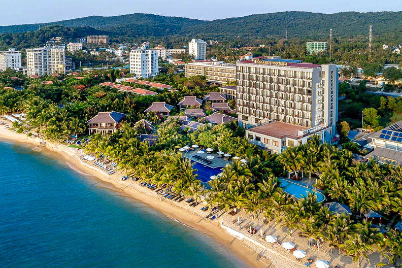 Widok z lotu ptaka na plażę z palmami, hotelami i błękitnym morzem.