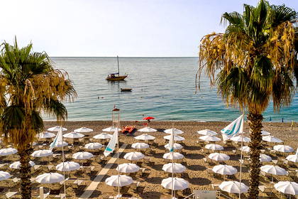 Plaża z palmami, białymi parasolami i łódką na morzu.