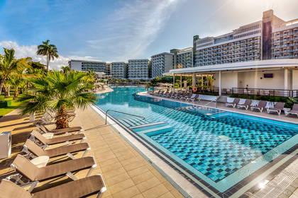 Duży basen w hotelu z leżakami i palmami wokół.