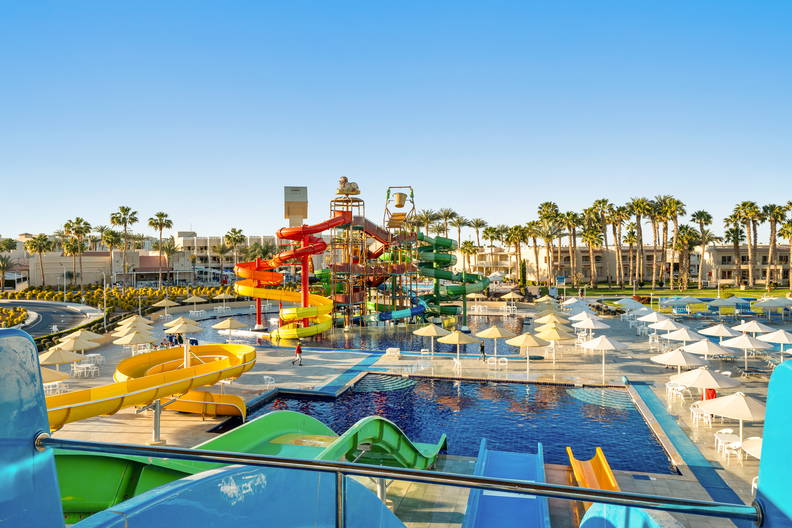 Kompleks basenów z kolorowymi zjeżdżalniami i palmami.