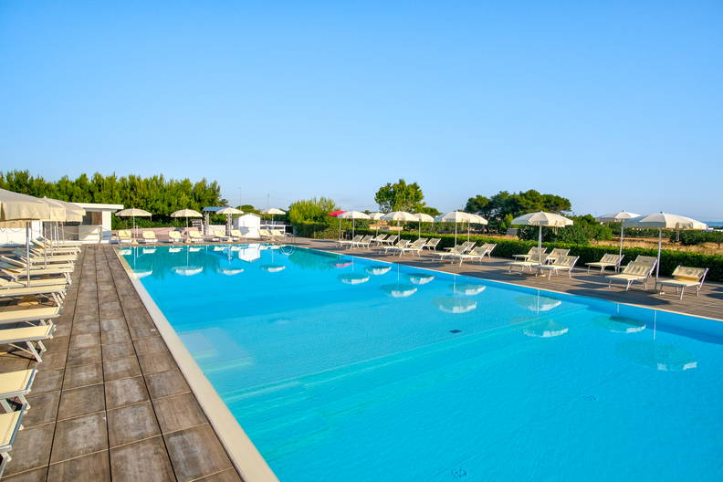 Basen z leżakami i parasolami w słoneczny dzień.