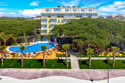 Hotel z basenem otoczony zielenią.