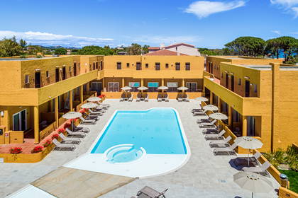 Hotel z basenem, leżakami i parasolami widziany z góry.