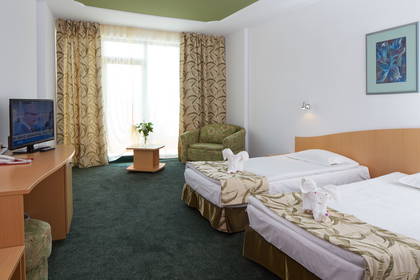 Pokój hotelowy z dwoma łóżkami, telewizorem i fotelami.