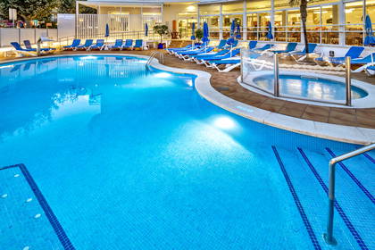 Basen z błękitną wodą i leżakami przy hotelu.