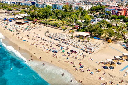 Widok z lotu ptaka na zatłoczoną, piaszczystą plażę i turkusowe morze z miastem w tle.