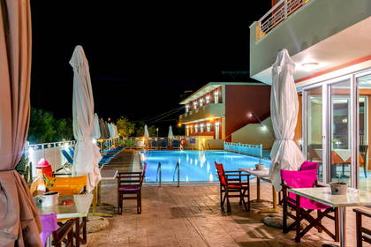 Oświetlony basen hotelowy i stoliki nocą.