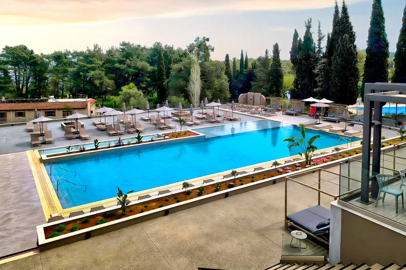 Duży basen z leżakami i parasolami w ośrodku wypoczynkowym na tle gęstego lasu.