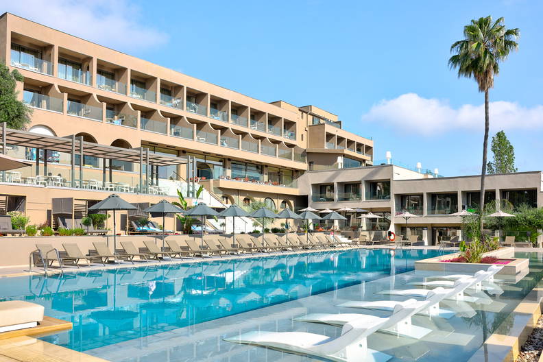 Nowoczesny hotel z dużym basenem, leżakami i parasolami w słoneczny dzień.
