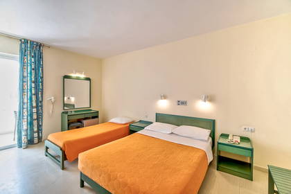 Pokój hotelowy z dwoma łóżkami i pomarańczowymi narzutami.