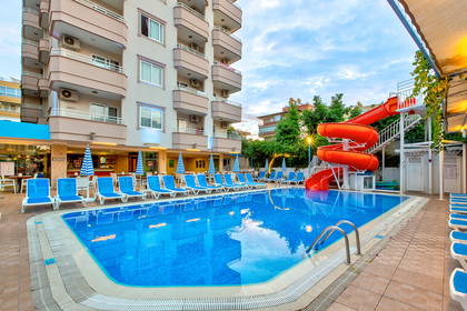 Hotelowy basen z niebieskimi leżakami i pomarańczową zjeżdżalnią wodną.