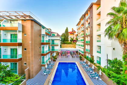 Hotelowy basen otoczony budynkami i palmami.