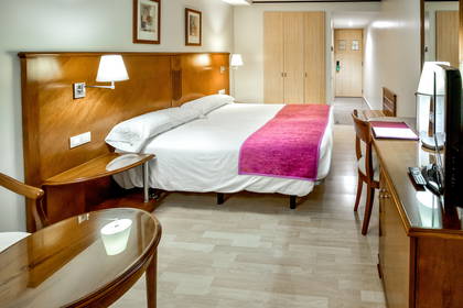 Pokój hotelowy z dużym łóżkiem, biurkiem i szafą.