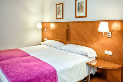 Pokój hotelowy z dwoma łóżkami, drewnianym zagłówkiem i szafką nocną.