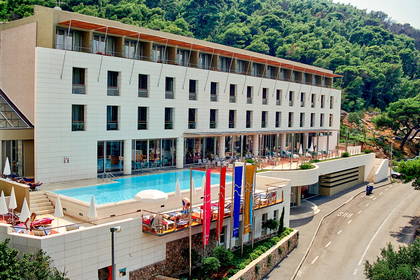 Wielopiętrowy hotel z basenem, leżakami i zielonym otoczeniem.