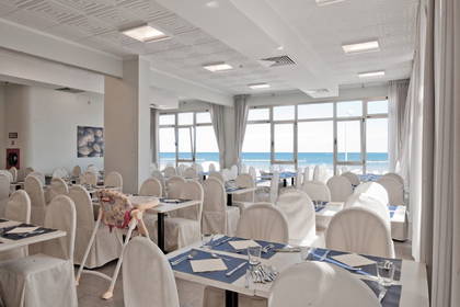 Restauracja z widokiem na morze. Na sali stoją nakryte stoły i białe krzesła.