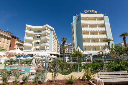Hotel Luxor z basenem otoczony zielenią w słoneczny dzień.