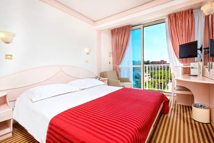 Pokój hotelowy z czerwonym łóżkiem, biurkiem i balkonem.