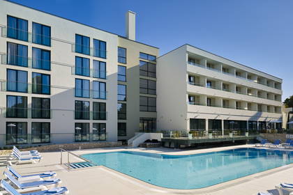 Hotel z basenem i leżakami w słoneczny dzień.