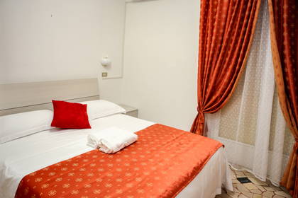 Pokój hotelowy z łóżkiem i pomarańczowymi zasłonami w oknach.