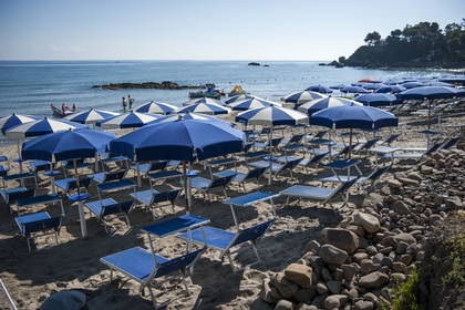 Plaża z niebiesko-białymi parasolami i leżakami.