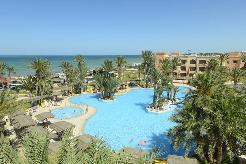 Hotel z basenem i palmami przy plaży, widok z góry.