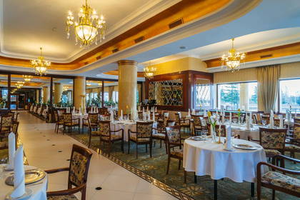 Sala restauracyjna z nakrytymi stołami oświetlona żyrandolami.