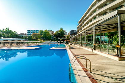 Hotelowy basen z leżakami i budynkiem w tle.
