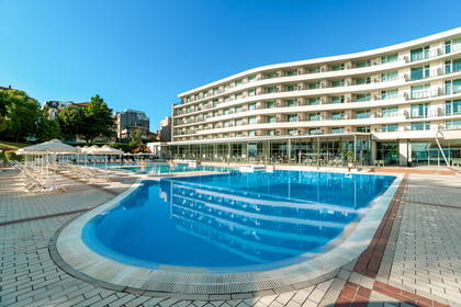 Hotel z basenem i leżakami w słoneczny dzień.