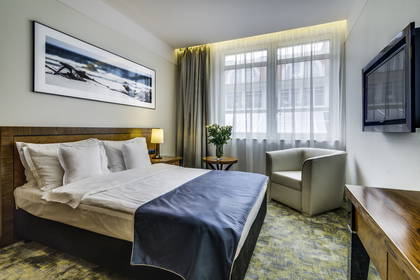 Pokój hotelowy z łóżkiem, fotelem i oknem.