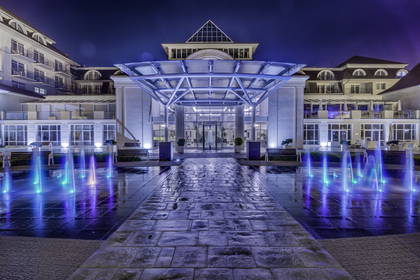 Hotel nocą z podświetloną fontanną i szklanym baldachimem.