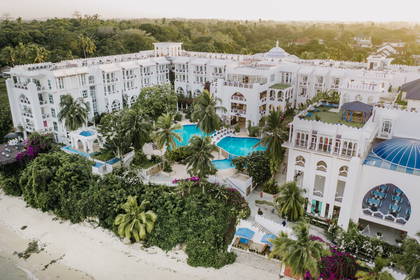Biały hotel z basenem i palmami, widok z lotu ptaka.
