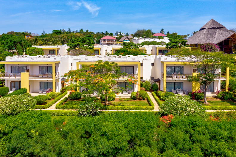 Kompleks hotelowy: białe budynki, zielone drzewa i błękitne niebo.