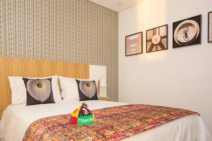 Pokój hotelowy z łóżkiem, poduszkami w kwiaty i kolorową narzutą.