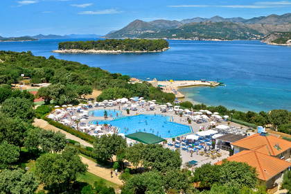 Widok z góry na kurort z basenem, plażą i wzgórzami w tle.