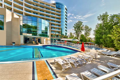 Kompleks hotelowy z basenem, leżakami i zielonym otoczeniem.