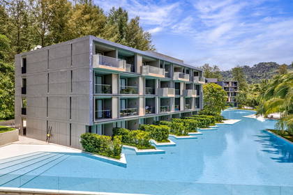 Nowoczesny, szary hotel z basenem otoczony zielenią.