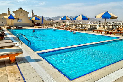 Basen na dachu hotelu z leżakami i parasolami przeciwsłonecznymi.