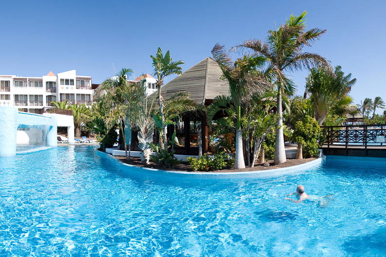 Basen z palmami i drewnianą altaną w ośrodku wypoczynkowym.