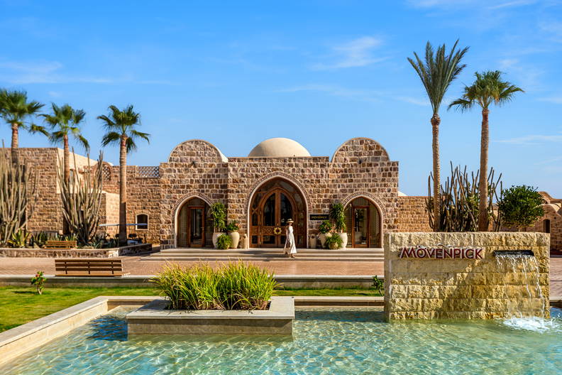 Fasada hotelu Mövenpick z palmami i fontanną na pierwszym planie.