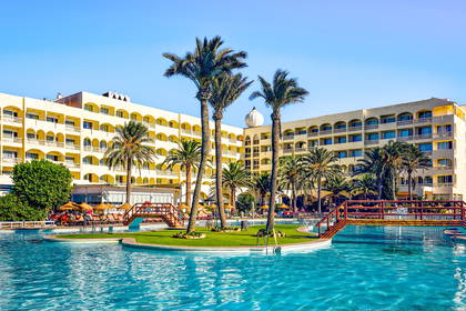 Hotel z basenem i palmami w słoneczny dzień.