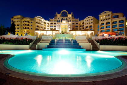 Oświetlony hotel z basenem nocą.