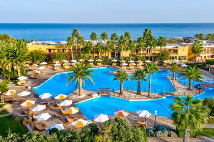 Hotel z basenem i palmami widziany z góry, w tle morze.